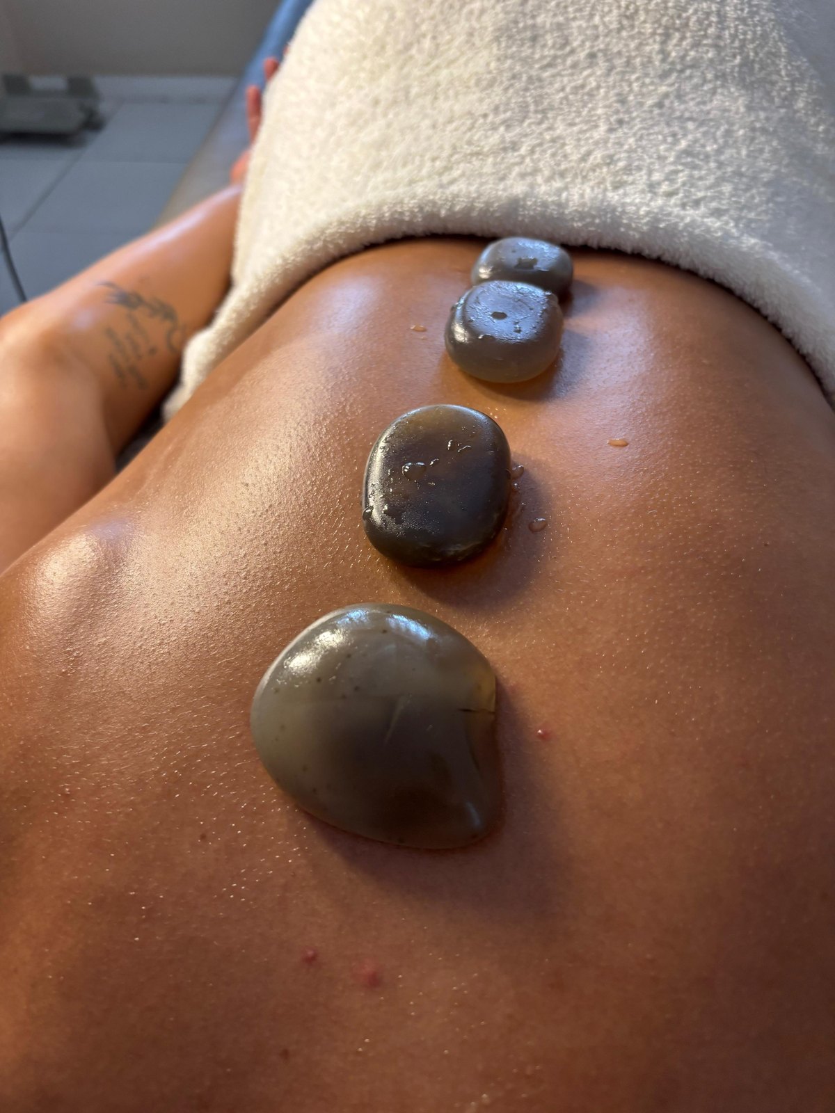 Massagem relaxante com pedras quentes sendo aplicada nas costas de uma cliente