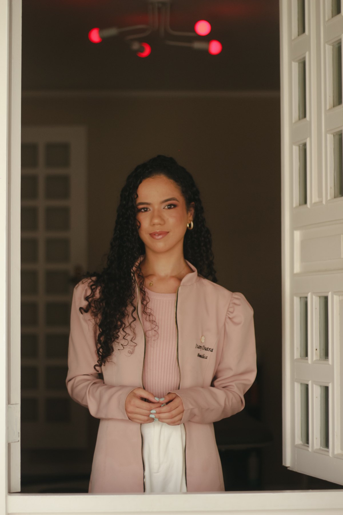 Itany, biomédica responsável pela Clínica Cristal, com jaleco rosa na entrada da clínica